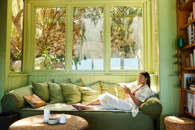 Young woman sitting on her sofa and texting on her phone