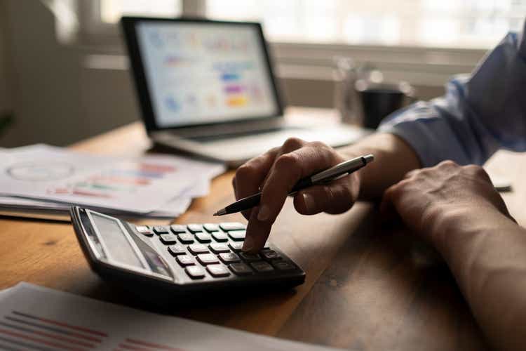 Business accounting concept, businessman using calculator with computer laptop, budget and loan documents in office.