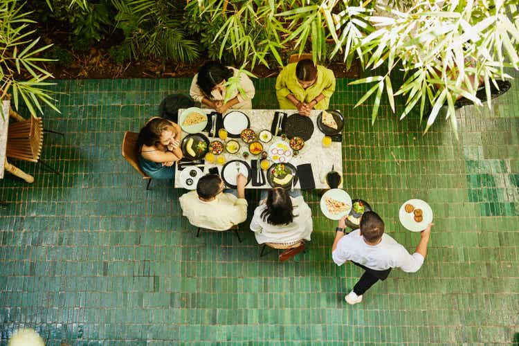 Wide shot of waiter bringing food to table of friends in restaurant