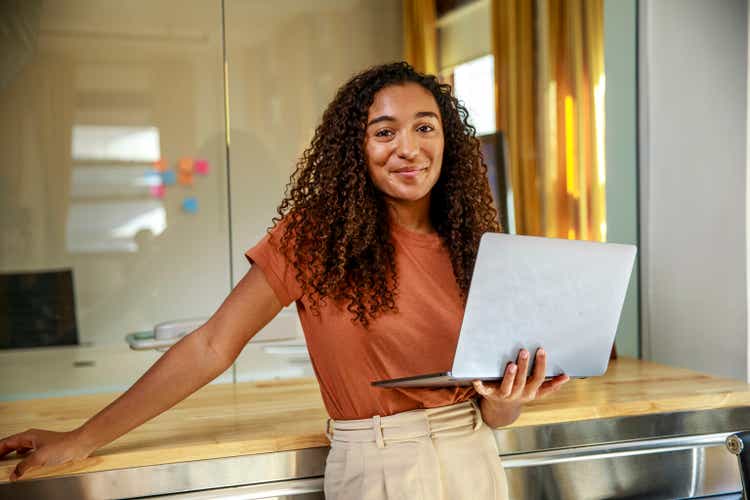 Smiling female entrepreneur with laptop standing in office