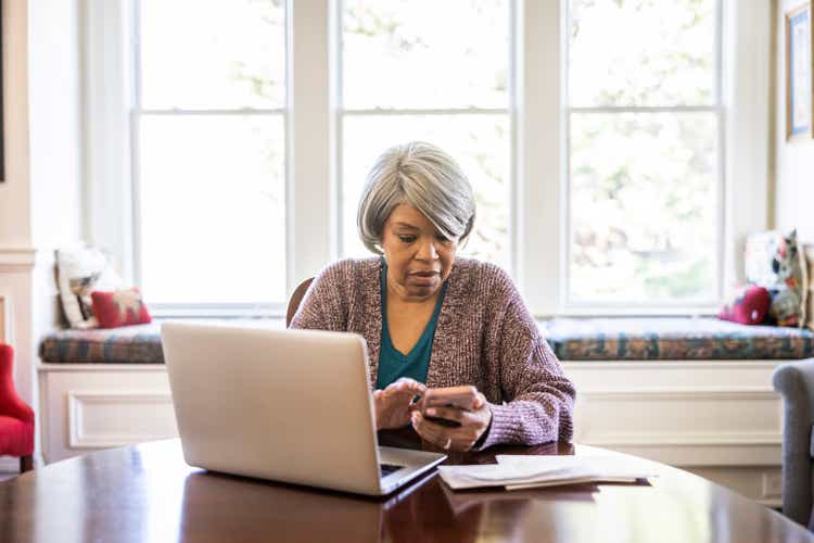 Senior woman paying bills with laptop and smartphone at home