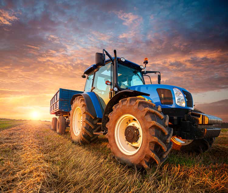 A tractor with a trailer on a stubble field waiting for grain to be loaded