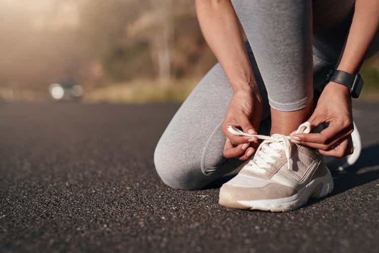 Fitness, the road and the woman connect her sneakers before the workout for the marathon, race or competition. Sports, workouts and female athlete are ready to start a healthy outdoor exercise for health