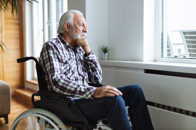 Lonely mature man in a wheelchair by the window at home
