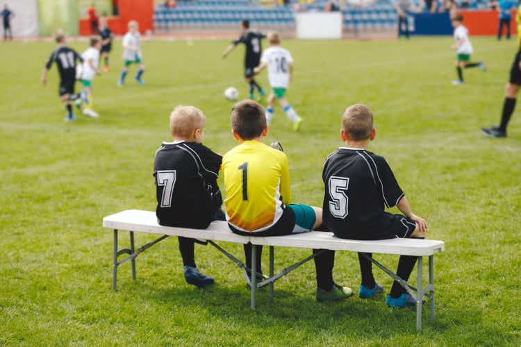 Young boys in soccer jerseys sitting on the substitute players" bench. Children play sports during school tournaments. Kids having fun attending sports competition