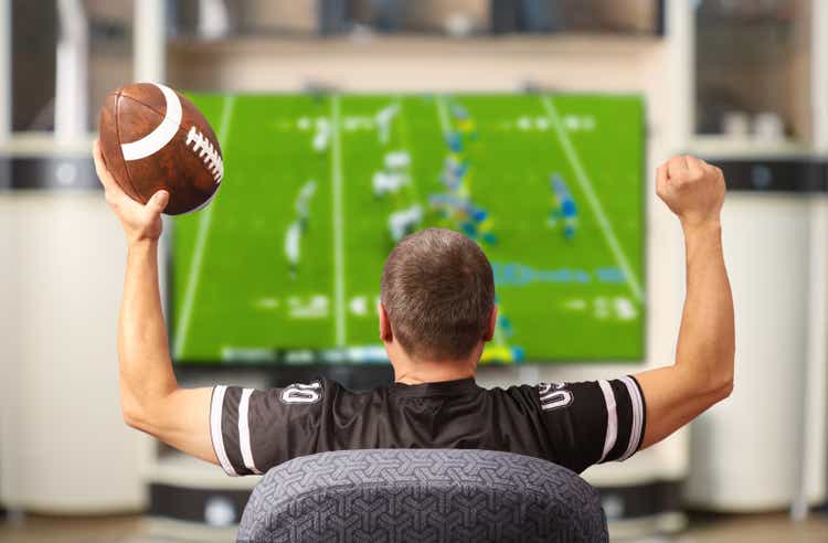 Fan of american football. Man with a ball watching TV.