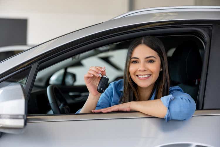 Happy woman holding the keys of her new car at the dealership