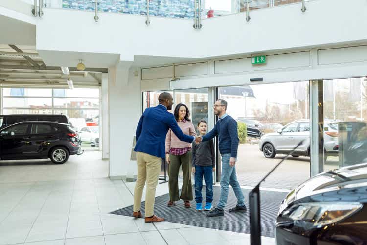 Automobile dealer shaking hands with family visiting a car showroom