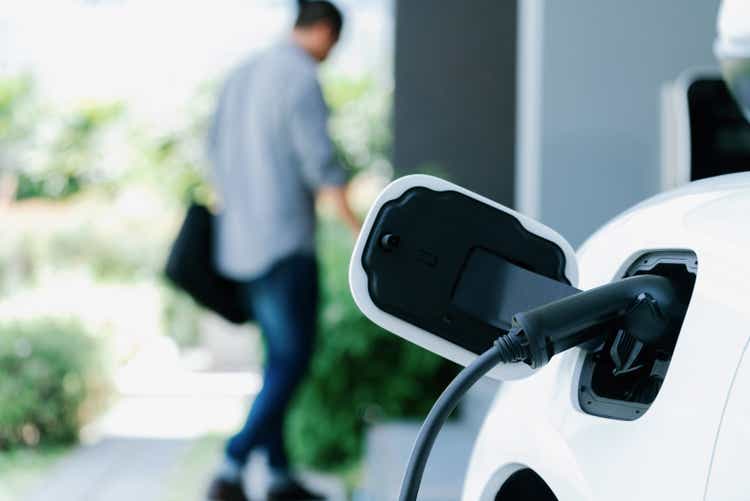 Focus EV charging station at home with blur progressive man in background.