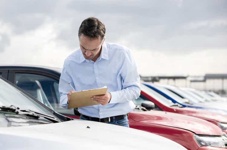 Car salesperson working at the dealership and taking notes on a clipboard