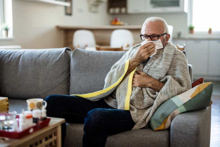 Senior man at home suffering with cold or flu virus. Shot of a senior man blowing his nose with a tissue at home.