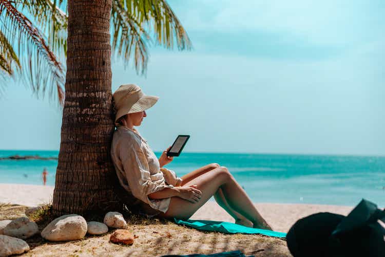 Woman with an e-reader on vacation at the beach reading a book