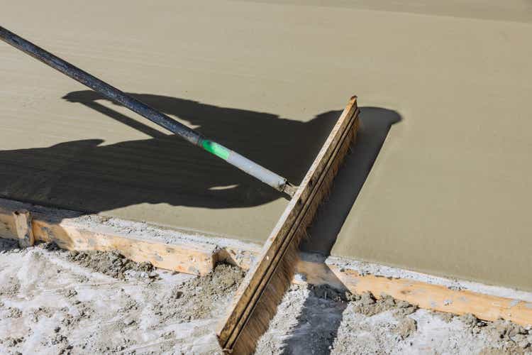 A construction laborer uses a broom to brush fresh wet concrete causing a groove texture pattern surface