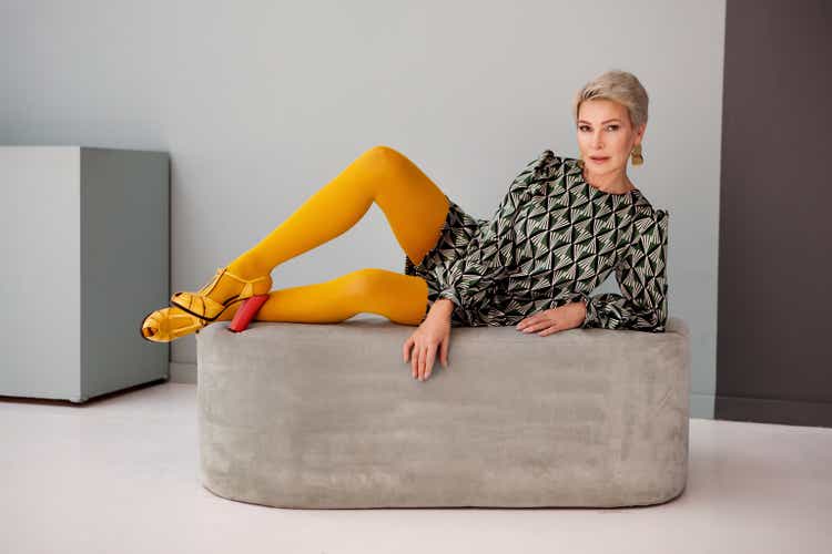 Sexy Mature fashionable woman short hair lying in studio, wear mini skirt and colorful yellow tights, high heeled sandals. Senior fashion model