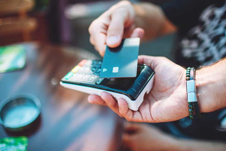 Adult man paying with credit card in cafe, closeup of hand using credit card and credit card reader