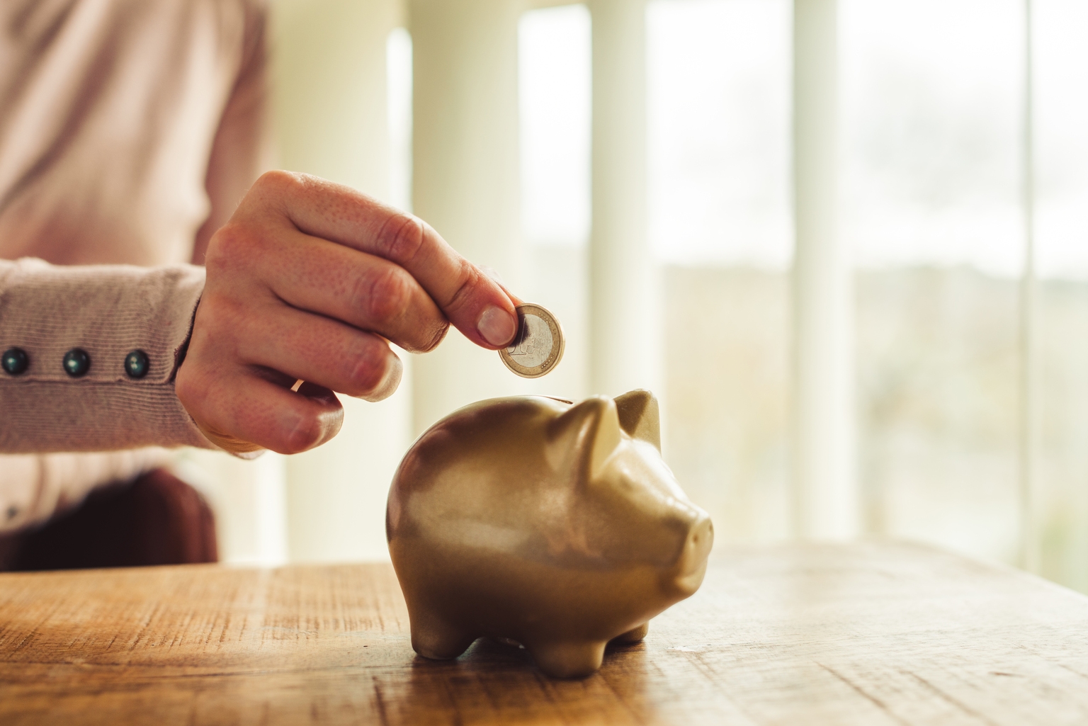 Woman putting savings in a golden piggy bank.