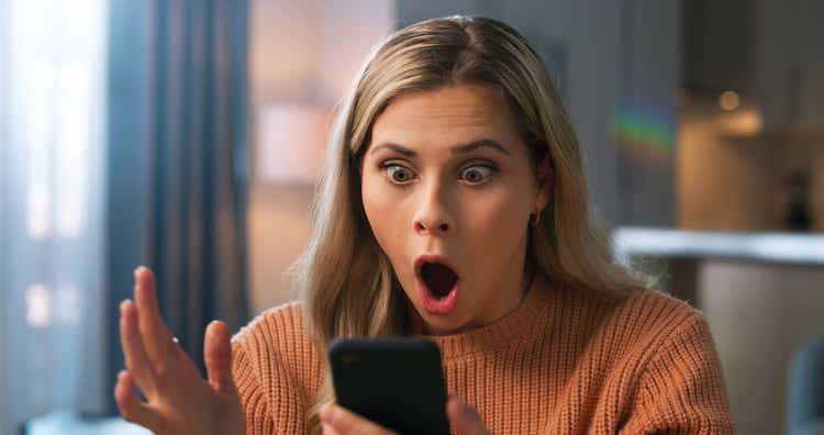 Shocked woman, face or what for phone scam, phishing email or security fail in house living room. Wow, anxiety or surprised person on mobile communication technology with hacker glitch or cyber theft