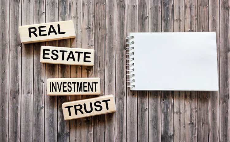 Conceptual words REIT real estate investment fund on wooden blocks on a wooden background next to a notepad for text.