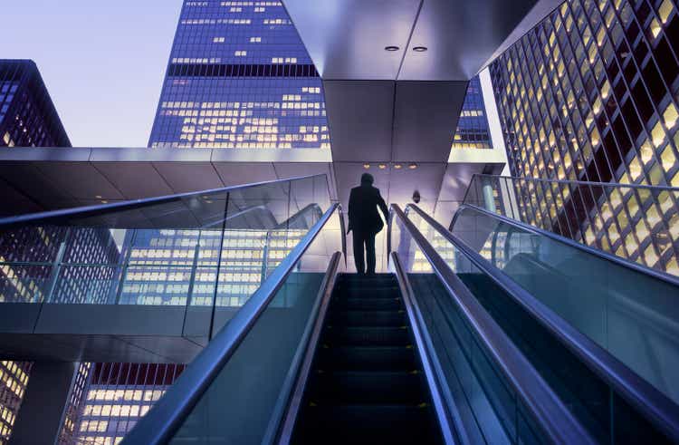 Businessman on top of moving escalator at modern illuminated business district