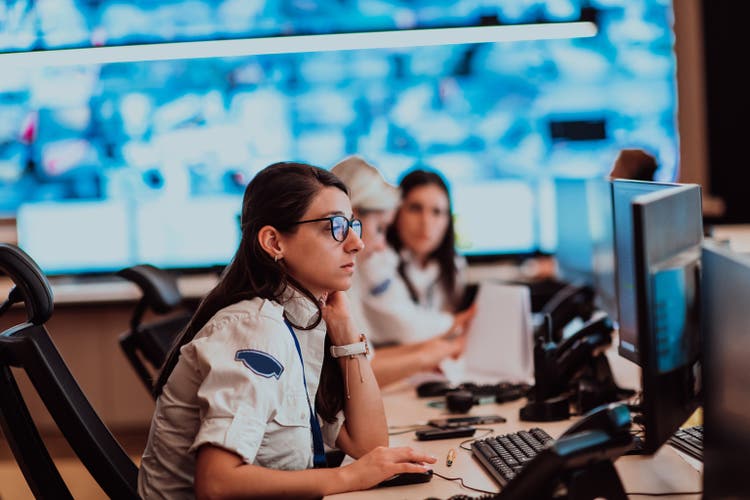 Group of Security data center operators working in a CCTV monitoring room looking on multiple monitors.Officers Monitoring Multiple Screens for Suspicious Activities