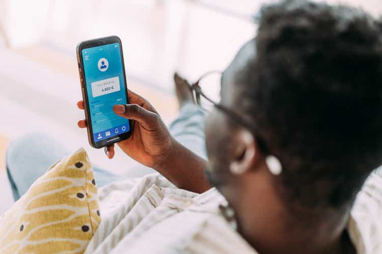 Young man using mobile app on smart phone for checking his finances while sitting on the sofa at home.