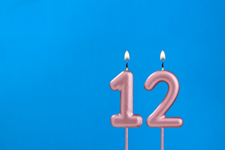Number 12 - Burning anniversary candle on blue foamy background