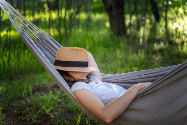 Woman resting in a hammock in a summer garden covering her face with a straw hat. Summer relax vacation