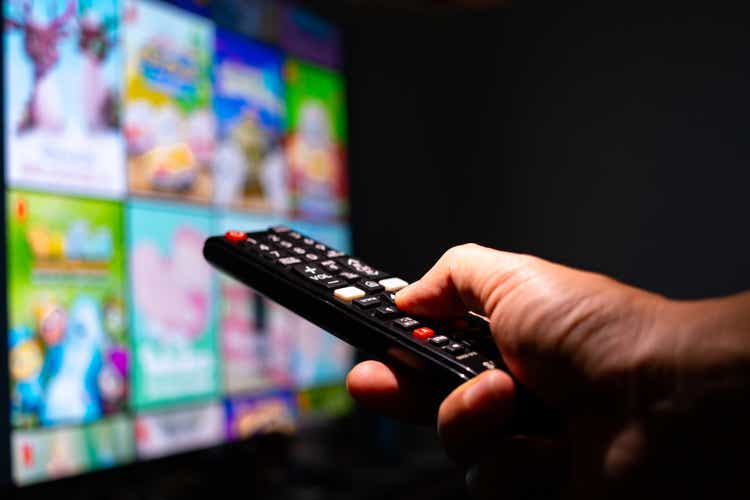Man"s hand holding a remote control, multimedia, online TV, broadcasting entertainment to viewers at home. The idea behind the broadcast