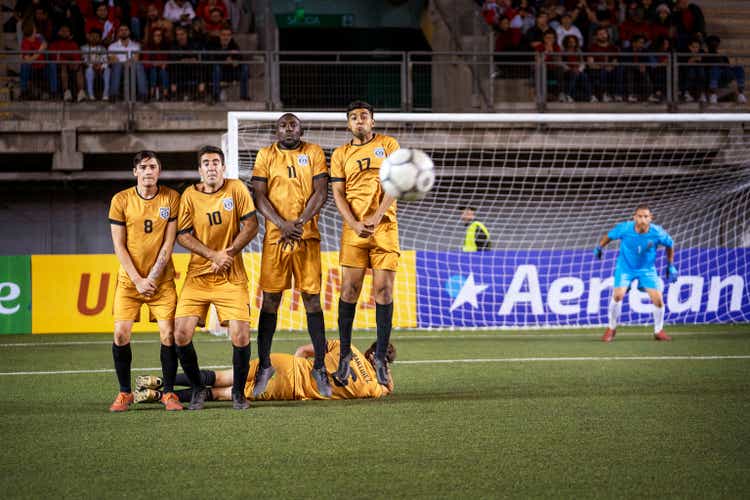 Professional soccer players form a free kick wall before ball heads toward them