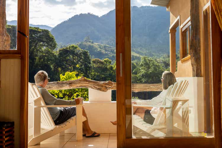 An older couple enjoying a cup of coffee on their deck overlooking the mountains.