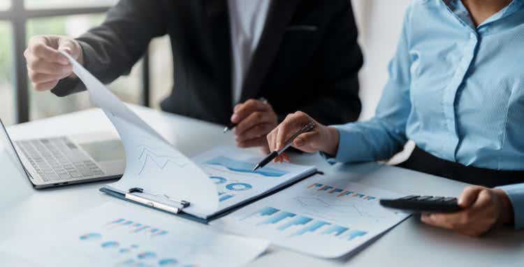Business people meeting to plan the financial market looking at past quarterly company graph and chart to compare investment and analyze company revenue and marketing strategy.