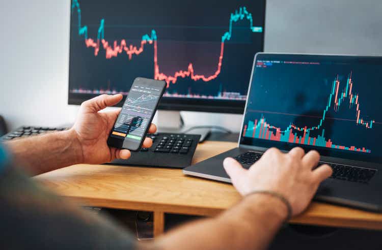 Man looking at currency trading app on his smart phone from his home office.