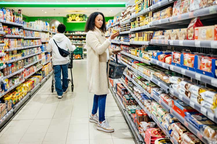 Woman Reading Item Label While Grocery Shopping In Local Supermarket