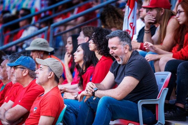 Older adult male in crowd of fans yawns and checks the time on his watch during big soccer match