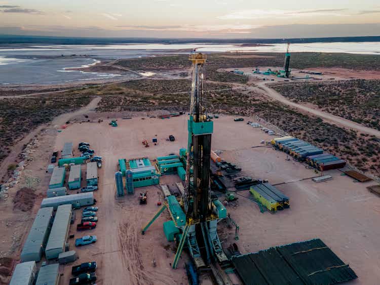 Drone captures a breathtaking sunset over the Permian Basin, showcasing an oil rig drilling and fracking for oil, amidst the vastness of the landscape