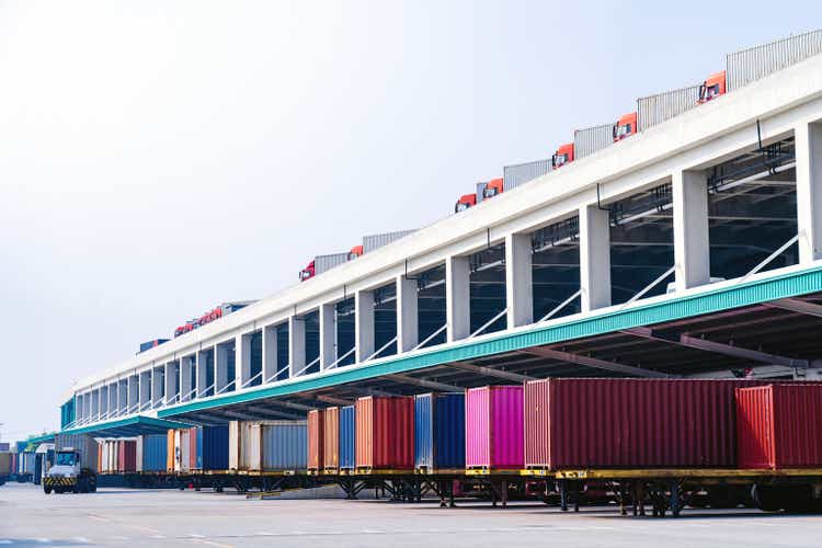 A huge number of large semi trucks are loaded and unloaded on the docks of a huge warehouse.  The semi-trailer with the already loaded trailer attached is detached and the trucker king of the road sets off again.