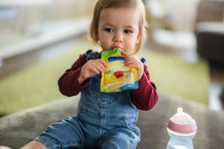 Cute little girl eating fruit puree in pouch