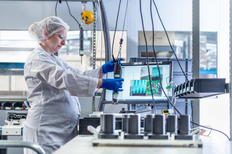 Pregnant assembly worker at work station in electronics factory clean room
