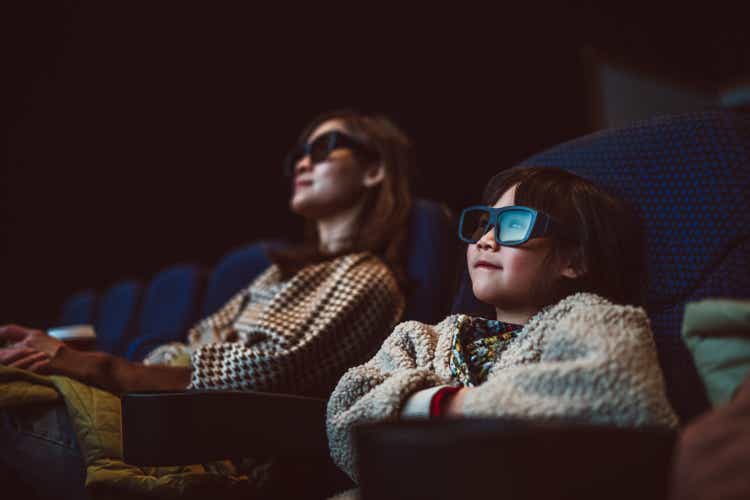 Mom & daughter watching movie with 3D glasses in cinema hall at movie theatre