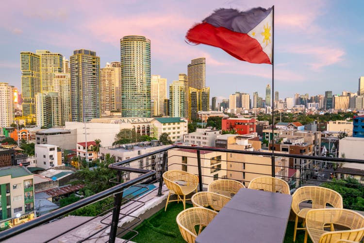 National flag of the Philippines,flying above a Makati rooftop,with backdrop of modern city skyline at sunset,Manilla,The Philippines.