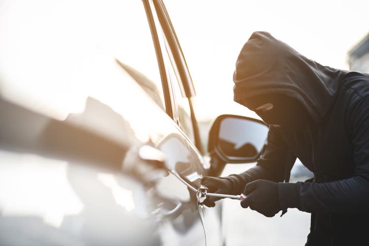 Close up car thief hand holding screwdriver tamper yank and glove black stealing automobile trying door handle to see if vehicle is unlocked trying to break into inside.