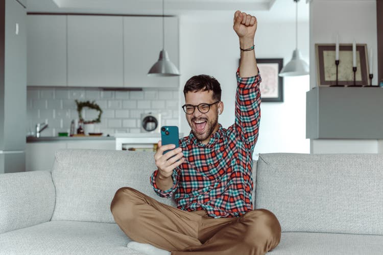A smiling man holding a mobile phone and celebrating success