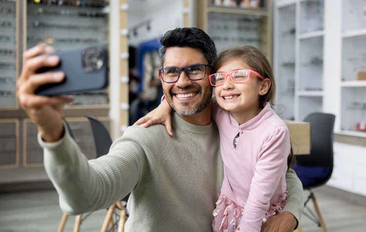 Father and daughter try on glasses and take selfie in optometry shop