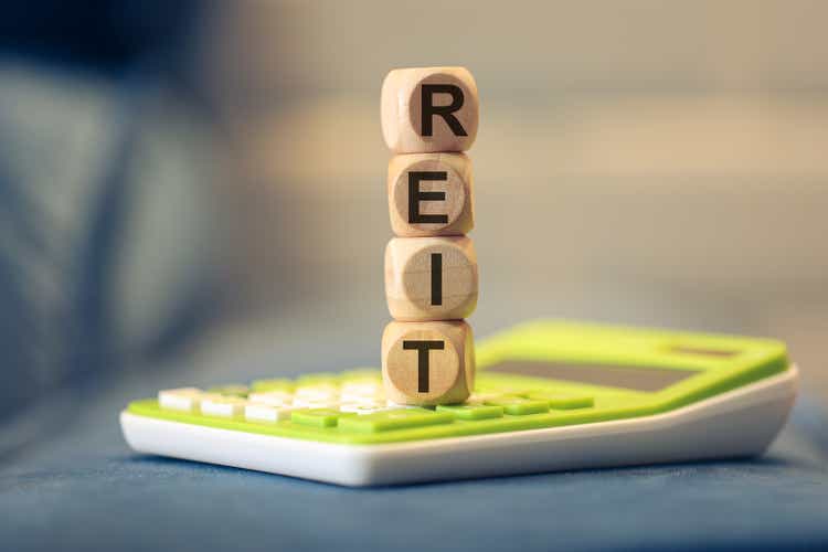 The acronym REIT for Real Estate Investment Trust written on wooden dice lying on top of a calculator.
