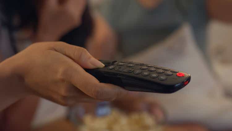 Close-up of Asian female friends on sofa click remote control to change TV channel and select favorite comedy or sitcom on online streaming at home at night. Leisure activities, lifestyle.