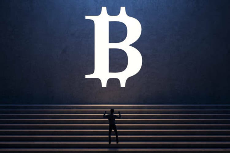 Back view of successful young businessman climbing stairs to white bitcoin sign on concrete wall background. Cryptocurrency and success concept.