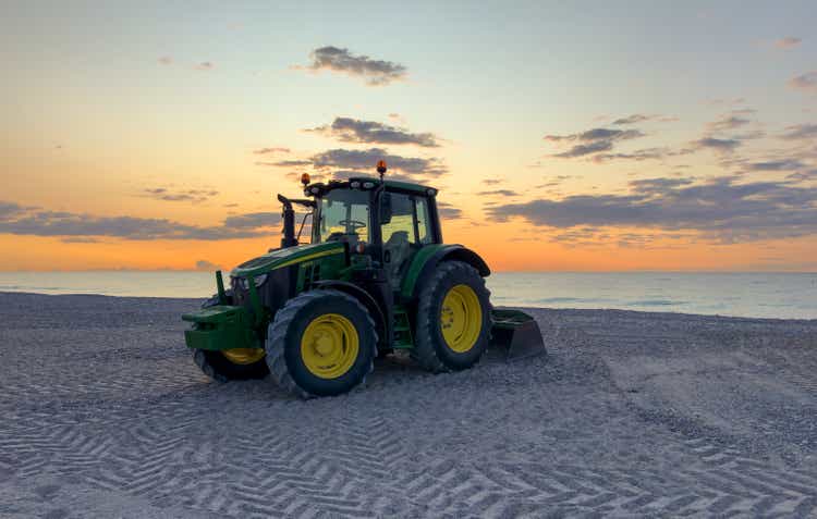 Clining beach and maintenance. John Deere tractor grooming sand on beach shore.