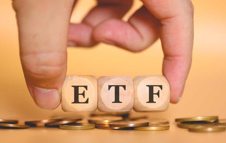 The acronym ETF for Exchange-traded fund written on wooden dice a man is holding. Coins in the composition. Studio photo.