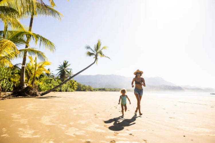 A mother and her daughter running down a palm tree scattered beach in Costa Rica.