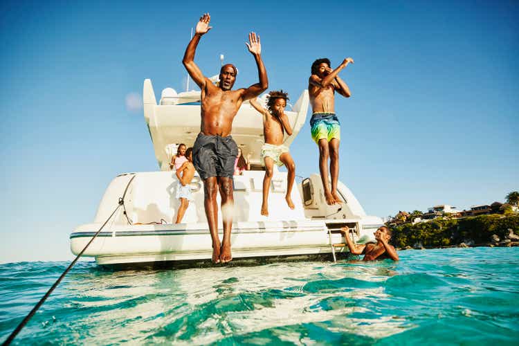 Wide shot father and sons jumping into water from swim deck of yacht